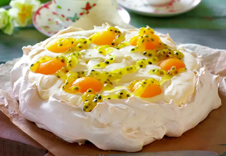 Eine Pavlova aus Baiser ist mit Lemon‑Curd‑Sahne gefüllt und mit Aprikosenhälften und Passionsfrucht dekoriert
