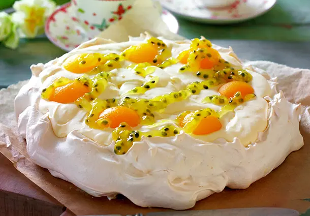 Eine Pavlova aus Baiser ist mit Lemon‑Curd‑Sahne gefüllt und mit Aprikosenhälften und Passionsfrucht dekoriert