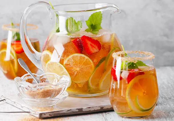 Großer Krug mit Zitronen-Limetten-Eistee, Eiswürfeln und frischen Zitrusscheiben steht auf einem Tisch.