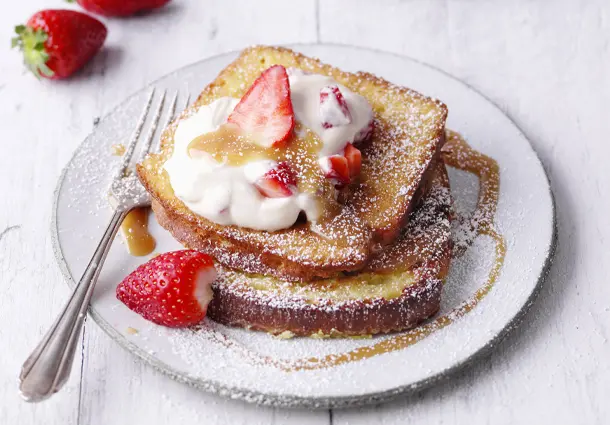 Goldbrauner French Toast mit cremigem Erdbeer-Karamell-Quark und frischen Erdbeeren ist mit Puderzucker bestäubt.