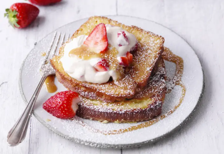 Goldbrauner French Toast mit cremigem Erdbeer-Karamell-Quark und frischen Erdbeeren ist mit Puderzucker bestäubt.