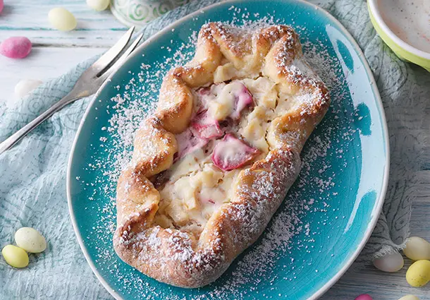 Kleine ovale Wähen aus Hefeteig, gefüllt mit Rhabarber- und Apfelstücken in einer Crème-fraîche-Creme, mit umgeschlagenem Rand und Puderzucker