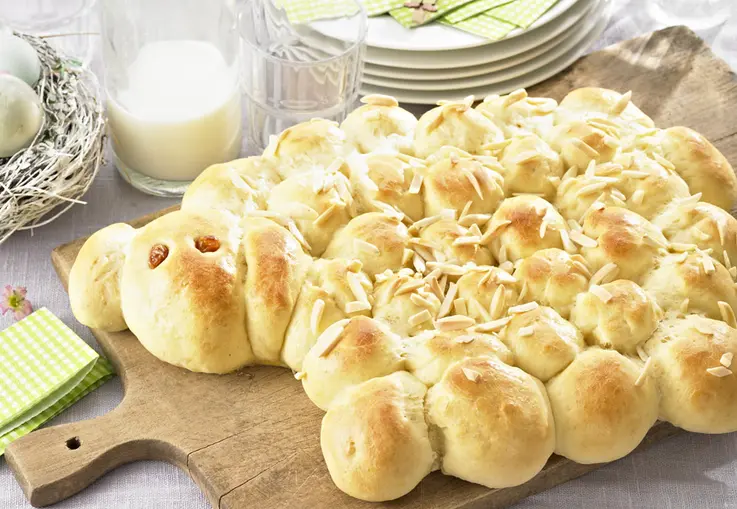 Ein aus Hefeteig geformtes Osterlamm aus vielen Teigbällchen, mit Rosinen als Augen und Mandelblättchen verziert, goldbraun gebacken