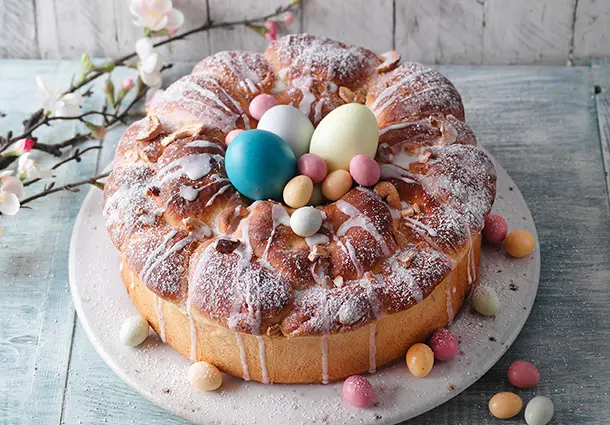 Ein ringförmiger Hefekranz aus Dinkelteig mit Cashew-Frischkäse-Füllung, orangefarbener Glasur und bunten Zucker-Ostereiern