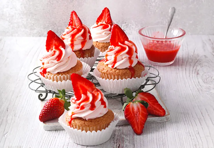 Cupcakes mit rosa Frosting, dekoriert mit Erdbeerscheiben und fruchtiger Sauce.