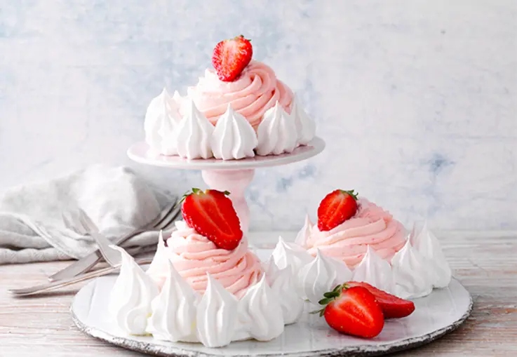 Knusprige Mini‑Meringueböden sind mit rosa Erdbeer‑Curd‑Sahne gefüllt und mit frischen Beeren und kleinen Baisertupfen dekoriert