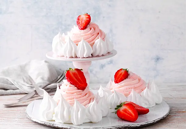Knusprige Mini‑Meringueböden sind mit rosa Erdbeer‑Curd‑Sahne gefüllt und mit frischen Beeren und kleinen Baisertupfen dekoriert