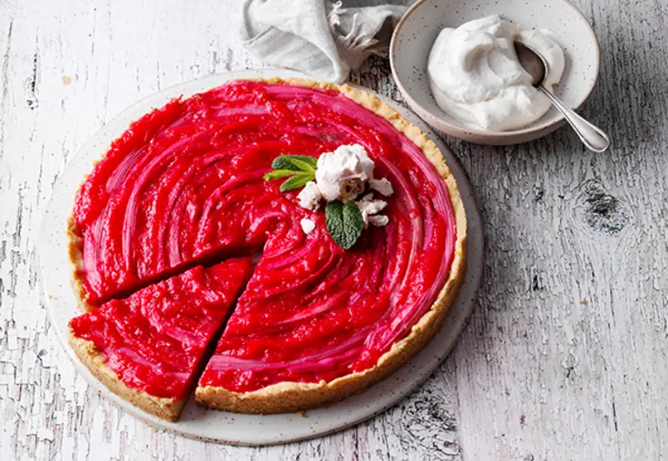 Eine Tarte mit Streuselboden und roten Rhabarberstangen, mit Minze und einem Baisertupfen garniert.