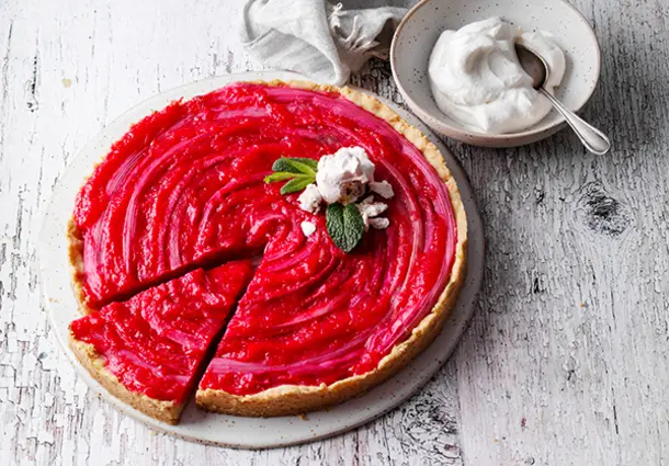 Eine Tarte mit Streuselboden und roten Rhabarberstangen, mit Minze und einem Baisertupfen garniert.