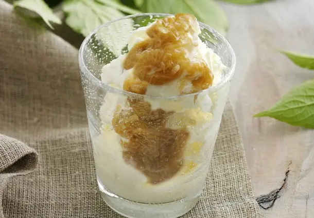Ein Glas Rhabarbersoße wird über Vanilleeis gegossen.
