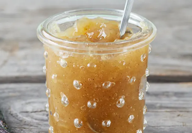 Ein Glas Rhabarberkonfitüre mit Kardamom und Vanille steht zwischen Rhabarberstangen und einer Vanilleschote.