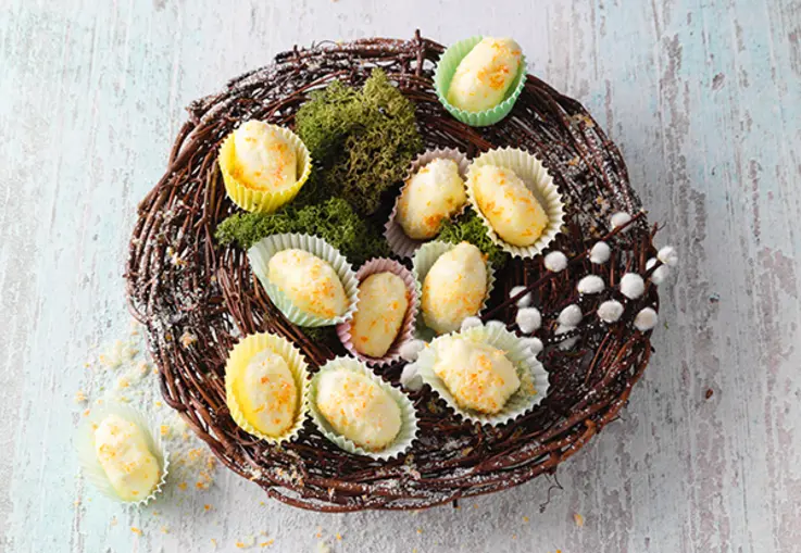 Kleine eierförmige Trüffel mit Eierlikör und Orangenaroma liegen in Papierförmchen in einem Nest aus Zweigen mit Moos