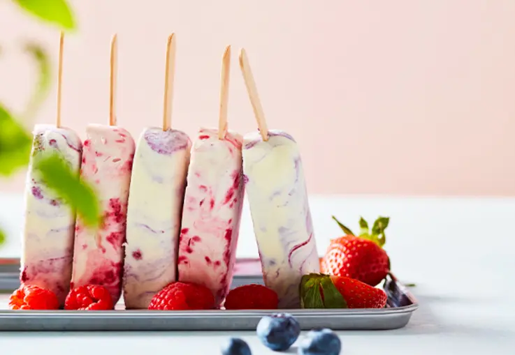 Stieleis in sahnigem Weiß zeigt violette Beerenswirls; die Marmorierung verläuft sanft und jedes Eis trägt einen unterschiedlichen Beerenton