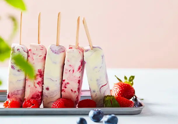 Stieleis in sahnigem Weiß zeigt violette Beerenswirls; die Marmorierung verläuft sanft und jedes Eis trägt einen unterschiedlichen Beerenton