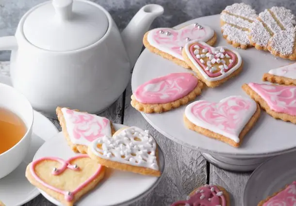 Verschieden geformte Butterplätzchen aus Mürbeteig, mit rosafarbenem und weißem Zuckerguss und Zuckerperlen dekoriert, auf einer Platte angerichtet