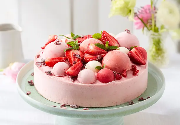 Ein gefrorener Erdbeer‑Rhabarber‑Cheesecake auf einem Teller, mit roten Fruchtschichten und Zitronenmelisse garniert.