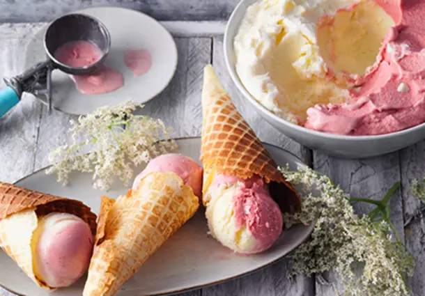 Selbstgemachte Waffelhörnchen mit Kugeln zartrosa Holunderblüten‑Erdbeereis, dekoriert mit Holunderblüten