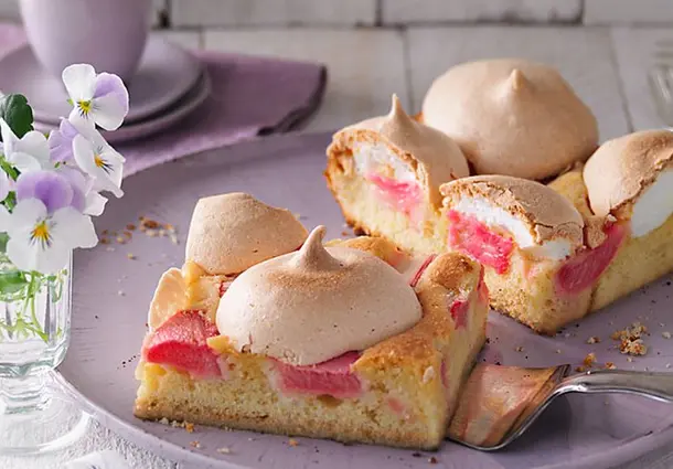 Quadratische Kuchenstücke mit saftigem Mandelteig, roten Rhabarberstücken und hellen Baiserhauben, auf einer Platte angerichtet