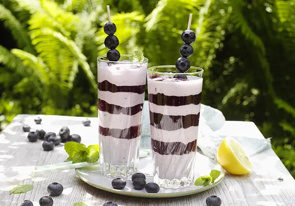 Gläser mit abwechselnden Schichten aus weißer Creme und dunkelviolettem Blaubeerpüree, dekoriert mit Beeren.