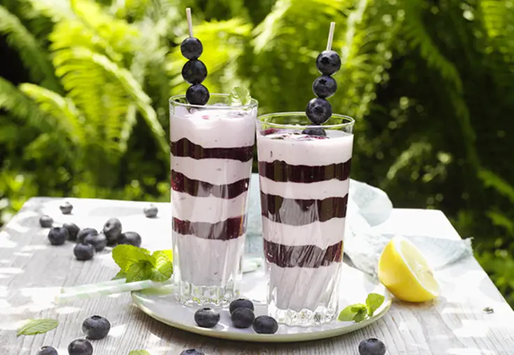 Gläser mit abwechselnden Schichten aus weißer Creme und dunkelviolettem Blaubeerpüree, dekoriert mit Beeren.