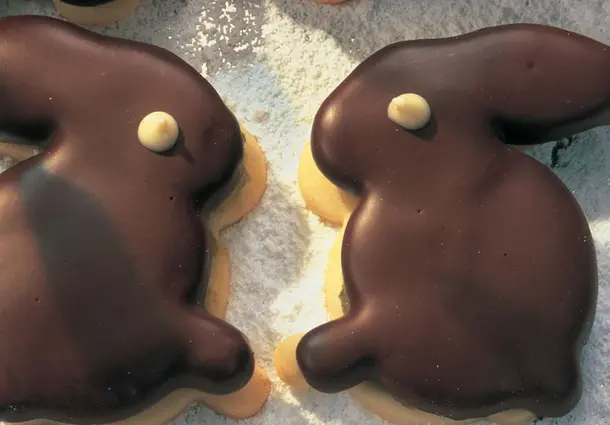 Biskuitartige Plätzchen in Hasenform mit einer Pistazien-Marzipan-Füllung, komplett in dunkle Kuvertüre getaucht und mit weißem Schokopunkt verziert