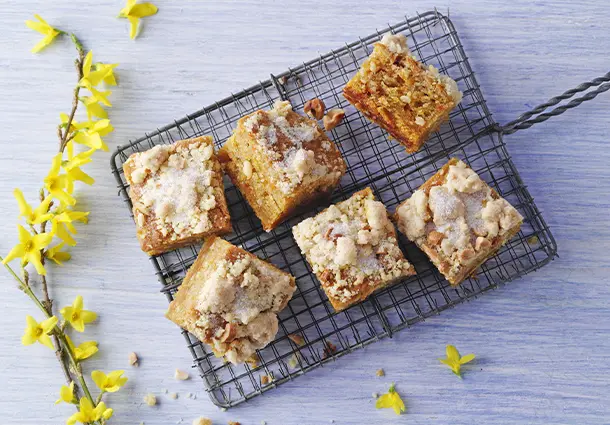 Kleine Stücke eines veganen Möhrenkuchens mit geriebenen Möhren, Apfelmus und knusprigen Cashewstreuseln, auf einem Kuchengitter angerichtet
