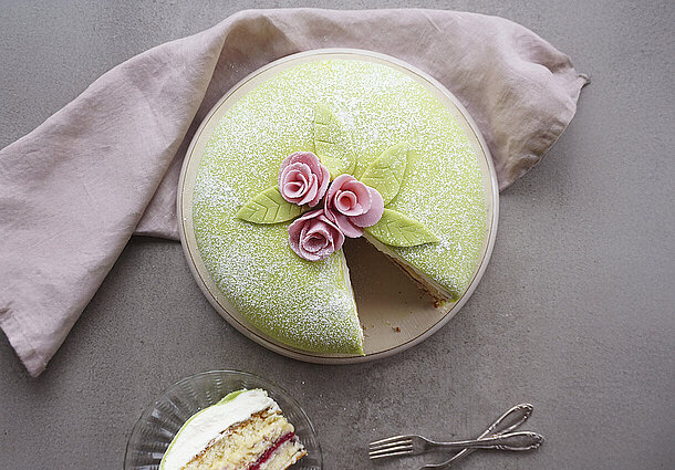 Runde Biskuittorte mit einer Füllung aus Himbeermarmelade und Vanillecreme verziert mit grünem Marzipan und Rosendekor