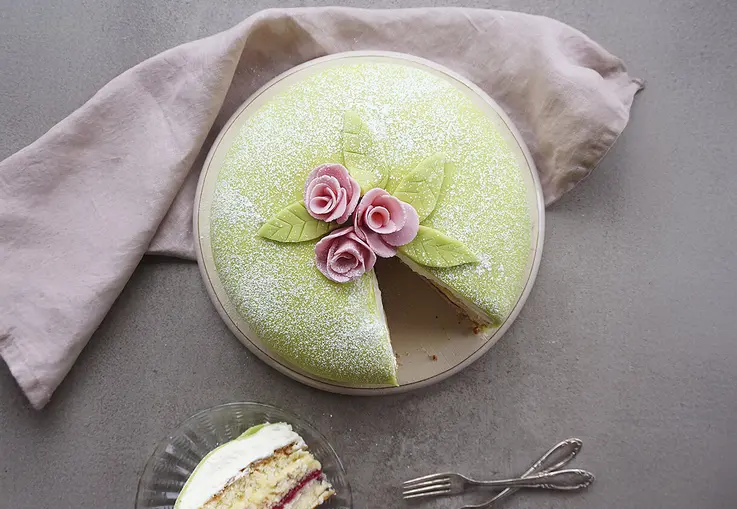 Runde Biskuittorte mit einer Füllung aus Himbeermarmelade und Vanillecreme verziert mit grünem Marzipan und Rosendekor