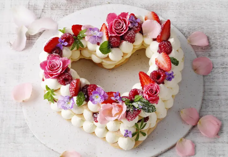 Herzförmiger Kuchen mit heller Oberfläche, überzogen mit Zitronenglasur und feinem Zuckerdekor in Form von Blüten