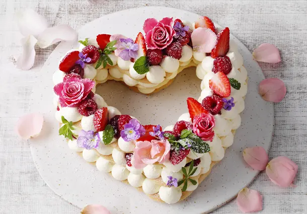 Herzförmiger Kuchen mit heller Oberfläche, überzogen mit Zitronenglasur und feinem Zuckerdekor in Form von Blüten